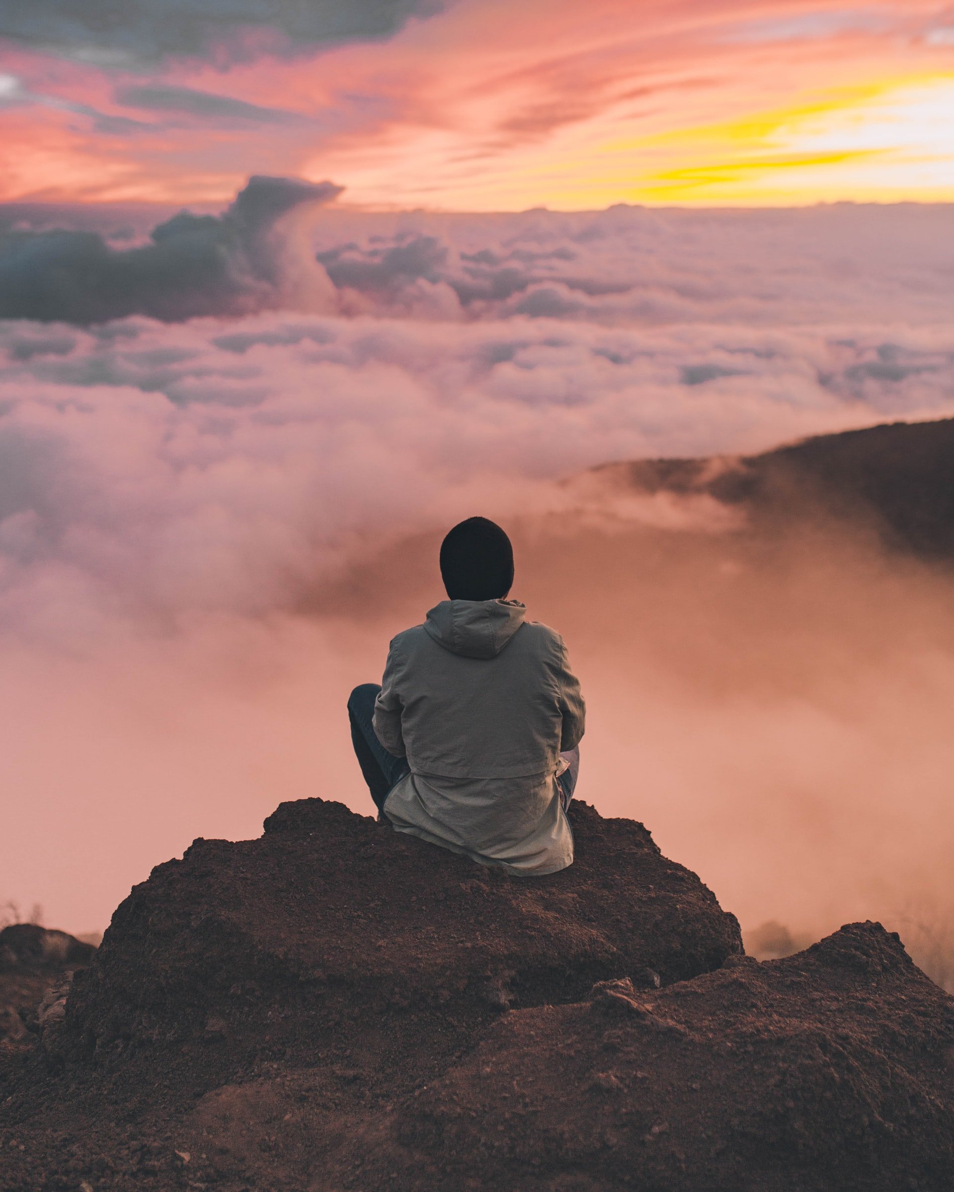 man sitting on a mountain top with sunrise in background